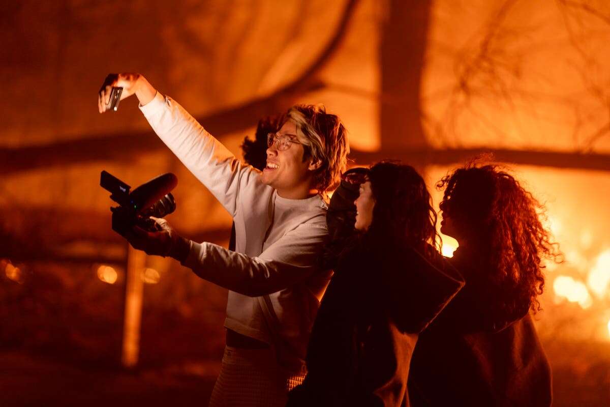 Young adults pose for smiling selfies by deadly California wildfires