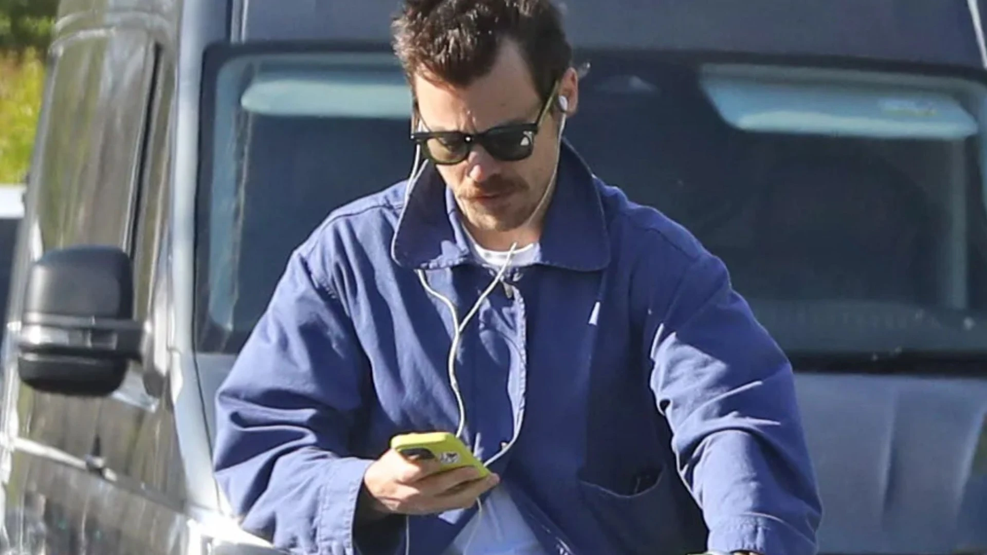Harry Styles looks down at phone while riding bike without helmet on busy road