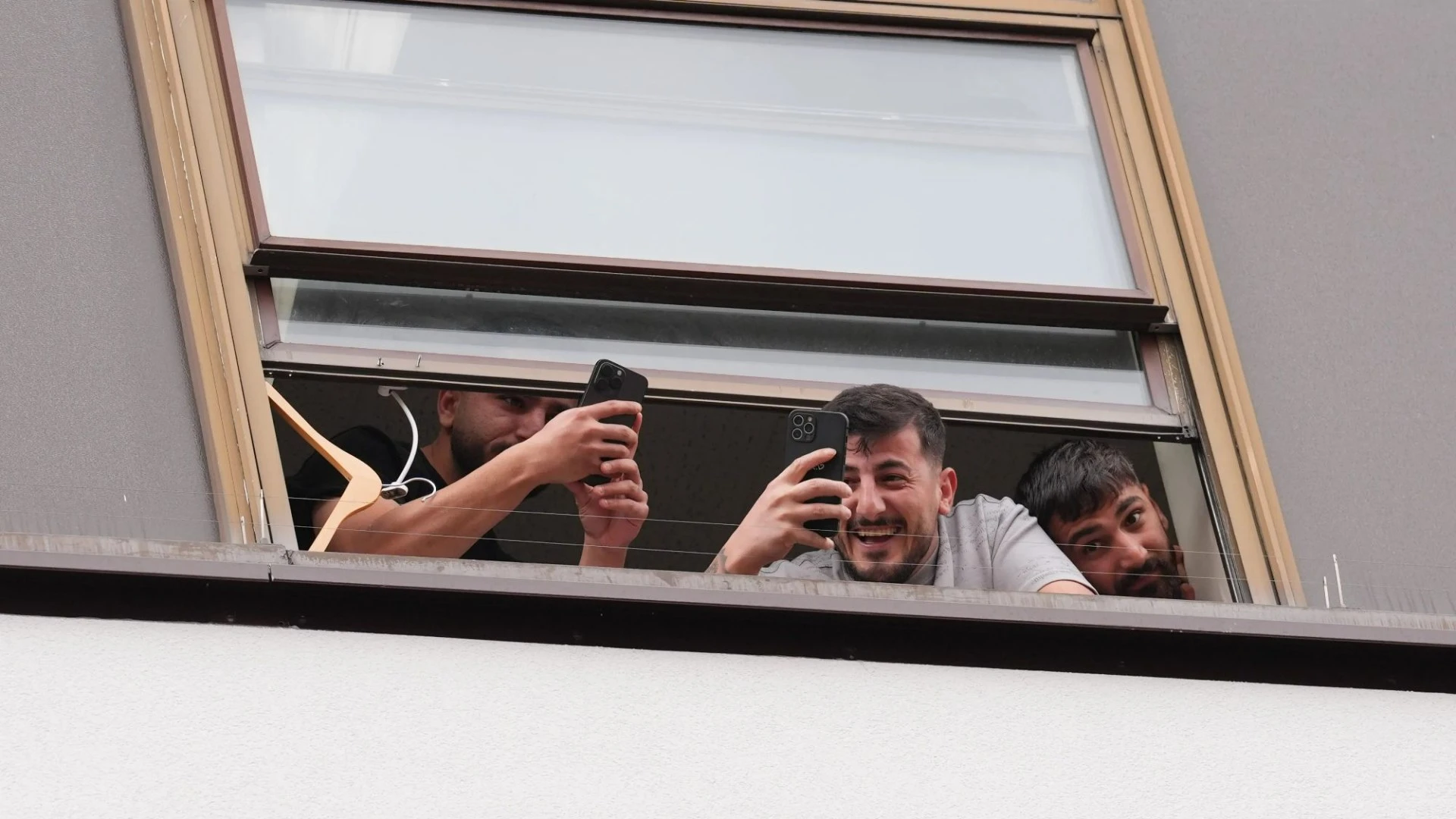 Migrants blow kisses from hotel window as they film protesters clashing with cops
