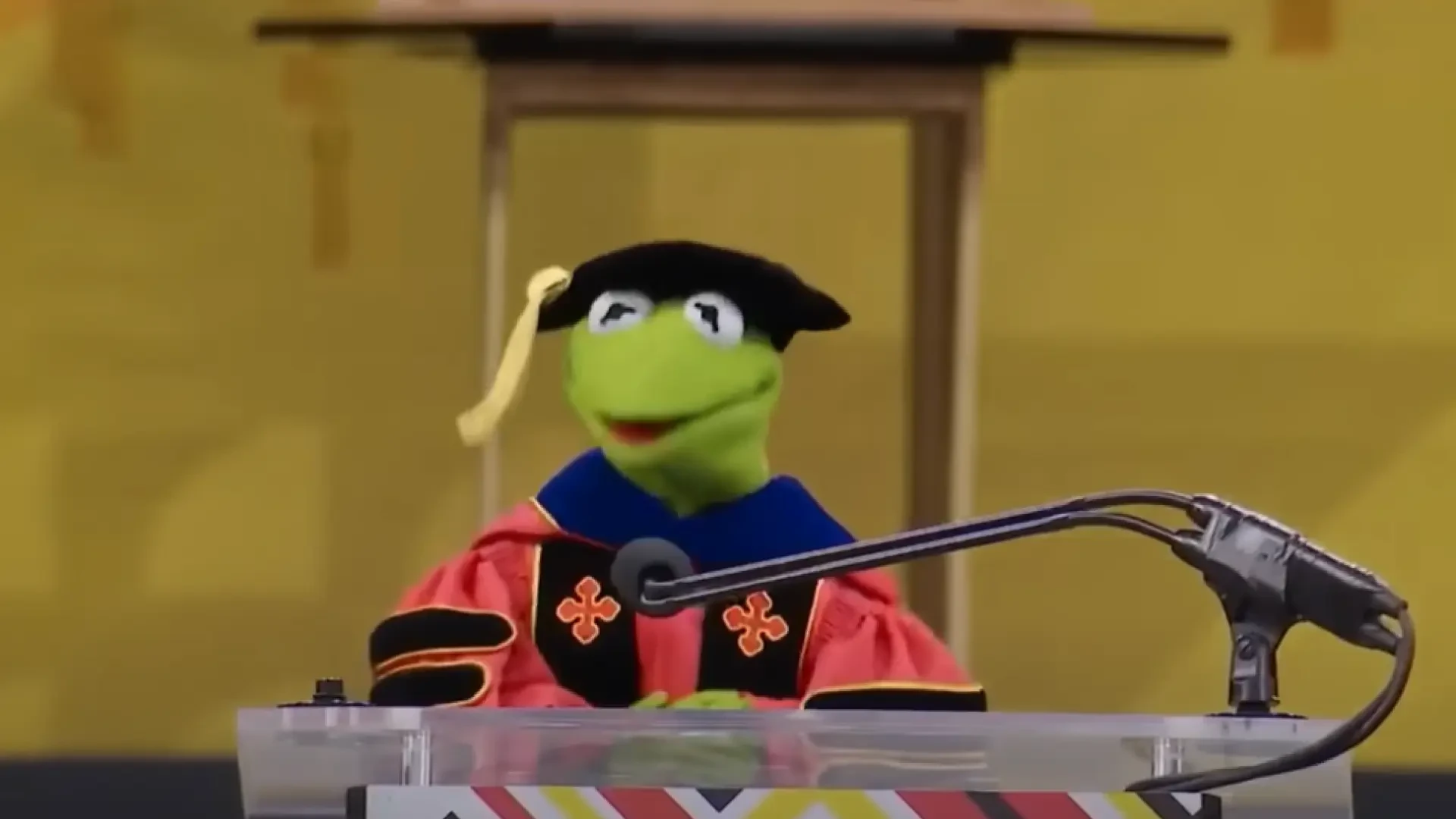 La rana Gustavo, con toga y birrete, da un integrador discurso de graduación en la universidad en la que su creador estudió