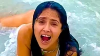 Salma Hayek celebrates World Oceans Day in white bathing suit as she laughs while getting knocked over by waves