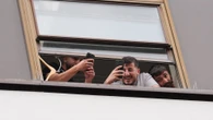 Migrants blow kisses from hotel window as they film protesters clashing with cops