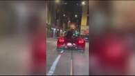 Seduto sul cofano di una Ferrari in movimento parla al telefono per le vie di Milano