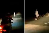 Creepy 'alien' figure with long limbs and pale skin walks along bridge at dead of night