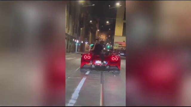 Seduto sul cofano di una Ferrari in movimento parla al telefono per le vie di Milano