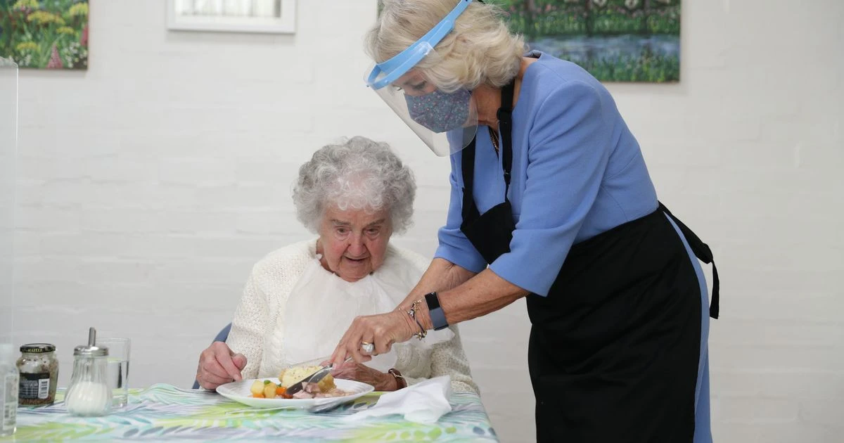 Camilla cuts up food for blind pensioner in visit to community centre to serve lunch